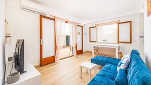 A modern living room with a blue sofa, a small white table, a TV, and a desk with a chair. - Felipe 1-4 Apartment with Terrace, Shared Pool & Wi-Fi (Tourist Taxes Included) (cala dor)