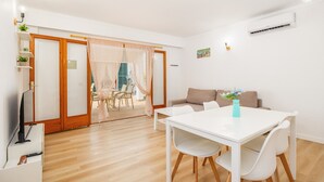 A modern living room with a white sofa, a dining table with chairs, a TV, and a ceiling fan. - Holiday Apartment "Felipe 2-2" with Terrace & Shared Pool (Tourist Taxes Included) (Cala Dor)