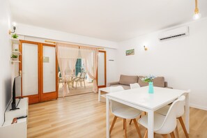 Un salon moderne avec un canapé blanc, une table à manger avec des chaises, un téléviseur et un ventilateur de plafond.