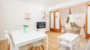 A modern room with a white table, chairs, a TV, and a sliding glass door leading to an outdoor area. - Holiday Apartment "Felipe 2-2" with Terrace & Shared Pool (Tourist Taxes Included) (Cala Dor)