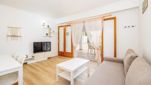 A modern living room with a white sofa, a white coffee table, a TV, and a dining area with a white table and chairs. - Holiday Apartment "Felipe 2-2" with Terrace & Shared Pool (Tourist Taxes Included) (Cala Dor)