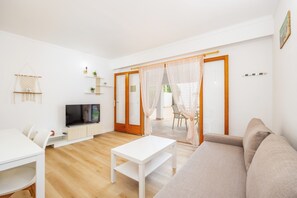 Un salon moderne avec un canapé blanc, une table basse blanche, un téléviseur et un coin repas comprenant une table et des chaises blanches.