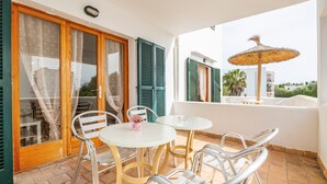 Un balcon avec une table et des chaises, un parasol en osier et une vue sur la mer.
