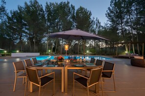 An outdoor dining area with a pool, surrounded by trees.