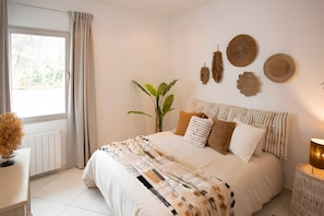 A bedroom with a bed, a bedside table, a lamp, a plant, and a window with curtains. - Villa "Can Drago" Private Pool, Large Garden, Terrace, WiFi & A/C (ibiza)