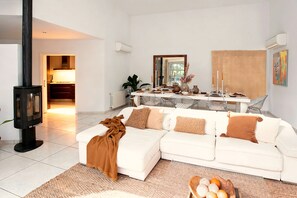 A modern living room with a white sofa, a fireplace, a dining area with a mirror, and a kitchen in the background. - Villa "Can Drago" Private Pool, Large Garden, Terrace, WiFi & A/C (ibiza)