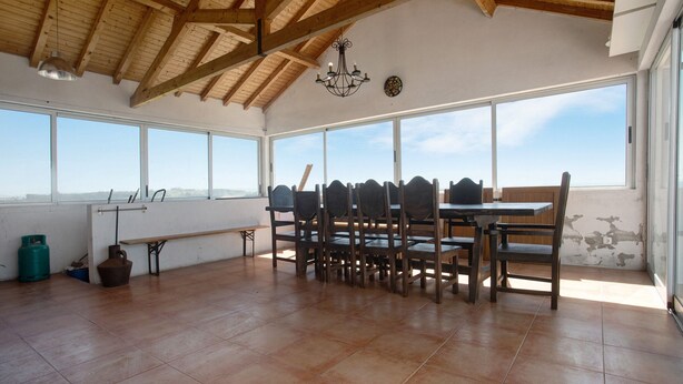 Una habitación espaciosa con techo alto, ventanas amplias, una mesa de comedor con sillas y un candelabro.