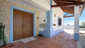 Un edificio con fachada de piedra, puertas de madera dobles, un patio empedrado y una pérgola.