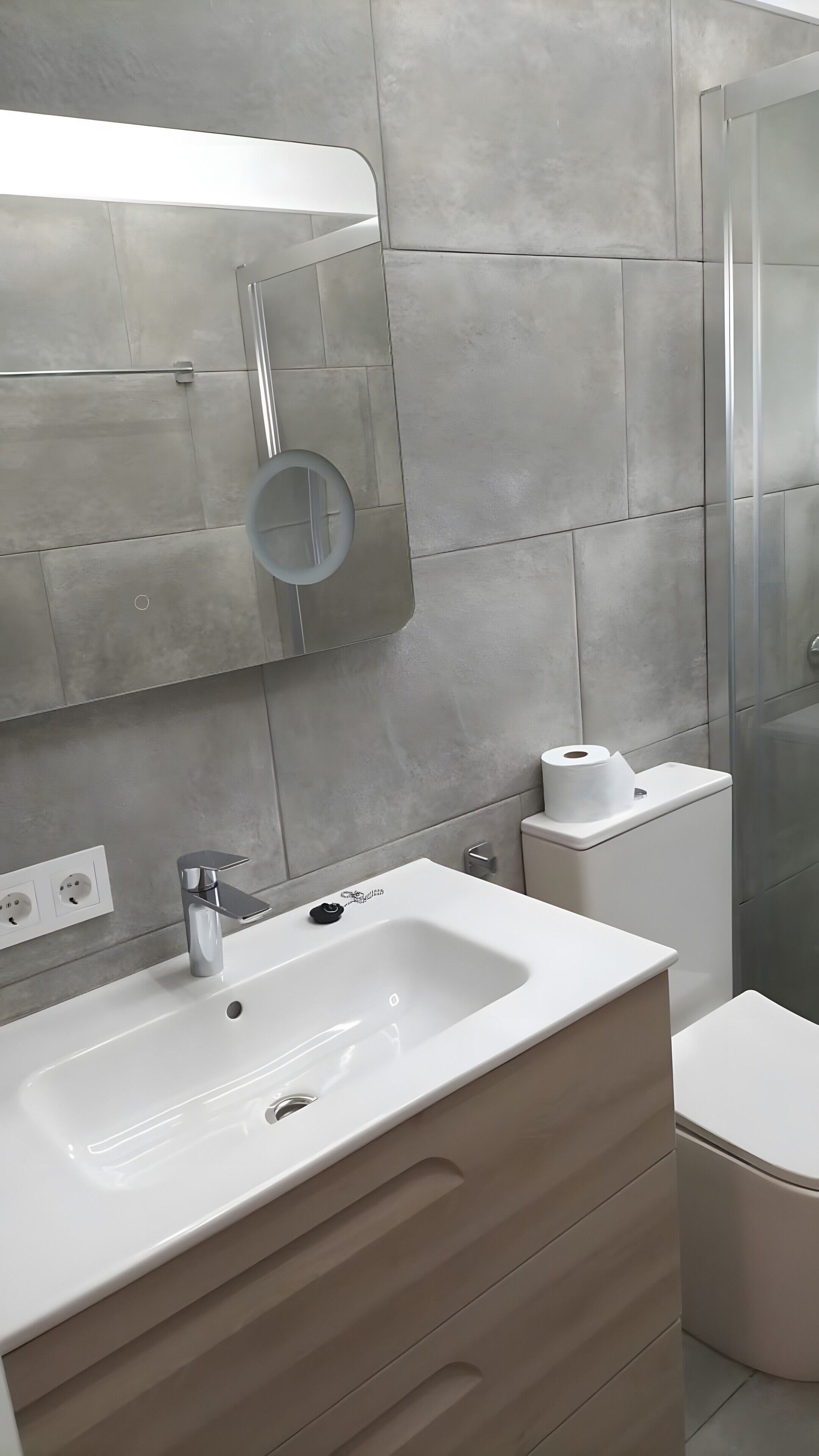 A modern bathroom with a white sink, a mirror, a toilet, and a glass shower enclosure.