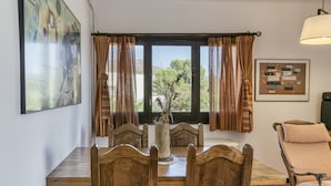 A dining area with a wooden table and chairs, a vase with dried plants, and a window with curtains. - Penthouse with Sea Views in Roses, with Sea Views, Terrace and Wi-Fi (El Mas Boscà)