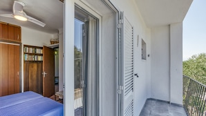 A balcony with a metal railing, a sliding glass door, a ceiling fan, and a bed with a blue bedspread. - Penthouse with Sea Views in Roses, with Sea Views, Terrace and Wi-Fi (El Mas Boscà)