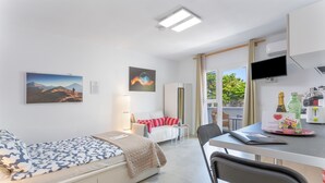 Een moderne hotelkamer met een bed, bureau, stoel, televisie en raam met uitzicht op groen.