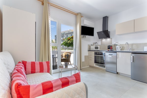 A modern kitchen with a flat-screen TV, stainless steel appliances, and a sliding glass door leading to a balcony.