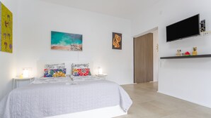 Ein modernes Schlafzimmer mit Bett, Kunstwerk, Fernseher und einer kleinen Ablagefläche.