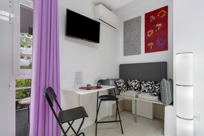 A compact room with a bed, a desk, a chair, a TV, and an air conditioning unit.