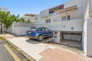 A building with a blue car parked in front, a sign for holiday rentals, and a gated entrance.
