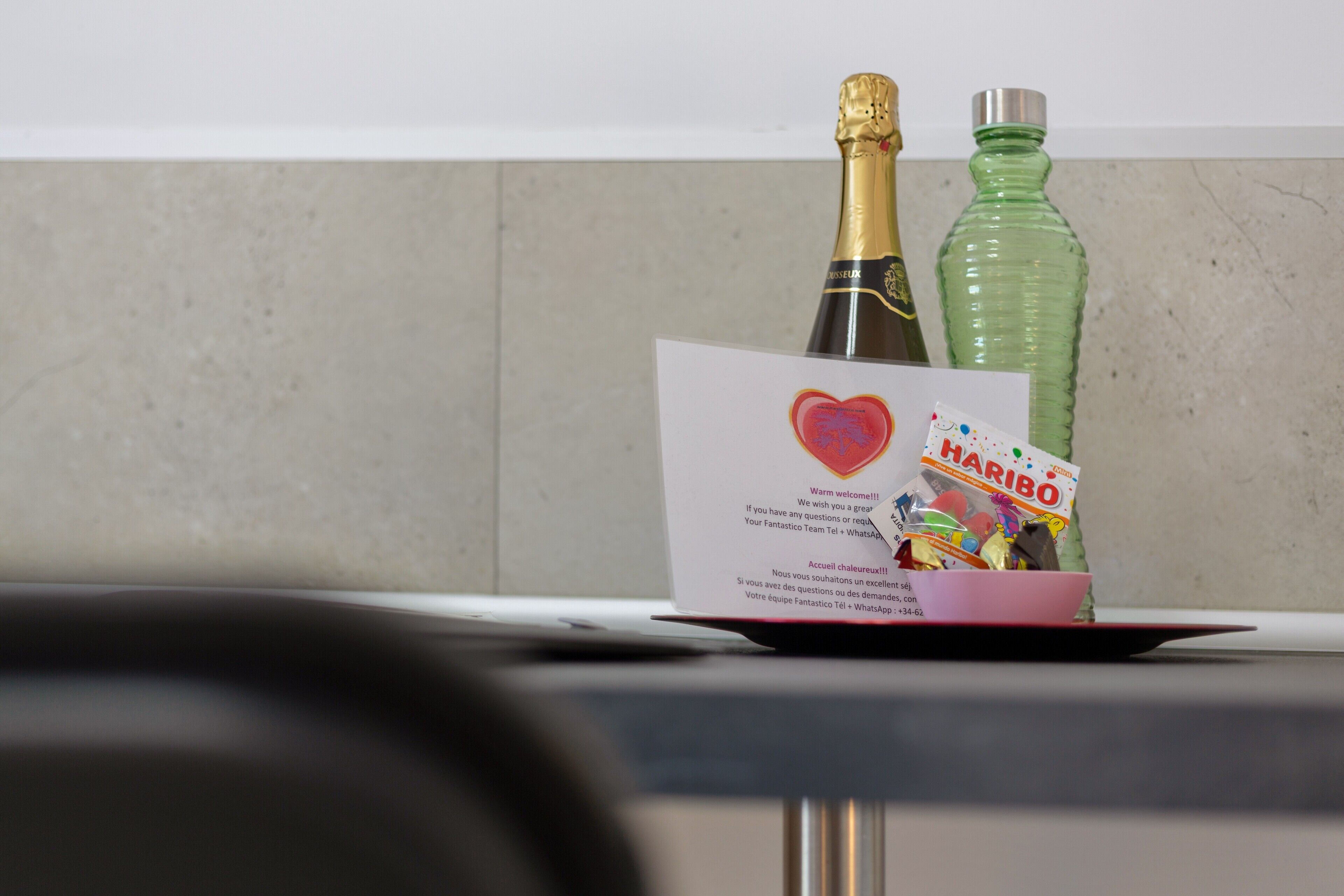 A bottle of champagne, a green bottle, and a card with a heart and text on a table.