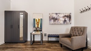 Ein modernes Wohnzimmer mit einem dunkelgrauen Kleiderschrank, einem Esstisch mit Stühlen, einem großen abstrakten Gemälde und einem gepolsterten Sessel.