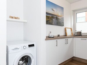 A laundry area with a Bosch washing machine, white cabinets, a wooden countertop, and a framed picture on the wall.