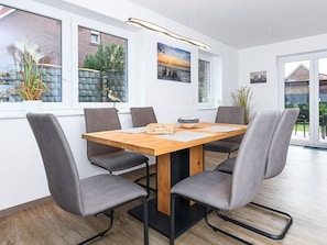 A modern dining area with a rectangular table, six grey upholstered chairs, and a wooden floor.