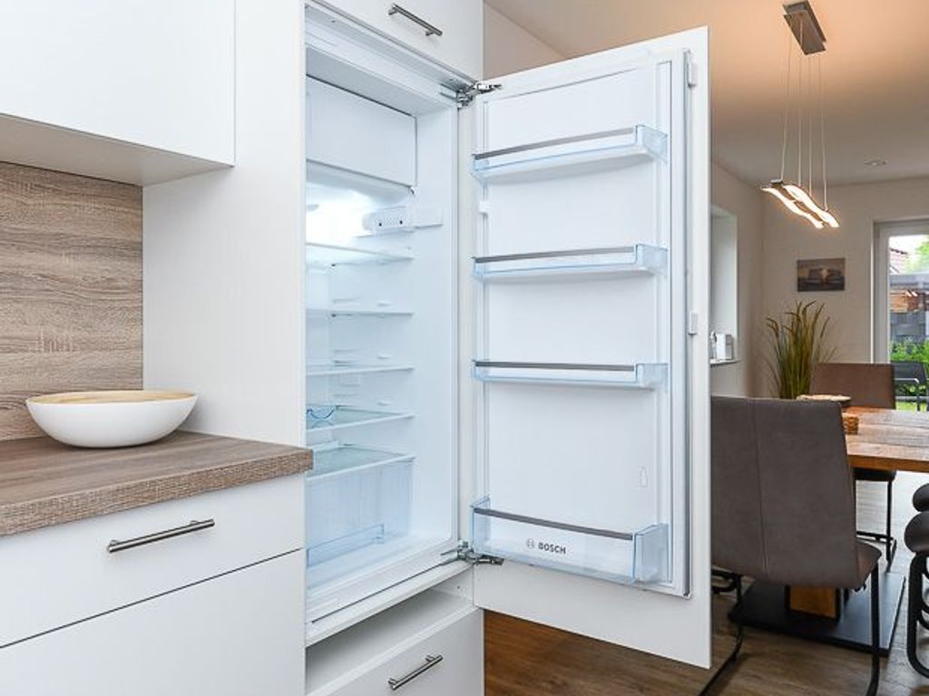 An open refrigerator with multiple shelves, a wooden countertop with a bowl, and a modern kitchen setting.