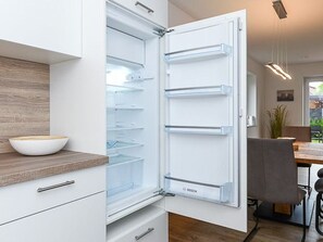An open refrigerator with multiple shelves, a wooden countertop with a bowl, and a modern kitchen setting. - Vacation Home in Meer, Germany (Dornum)