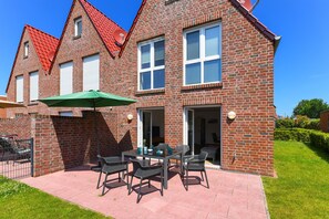 A two-story brick house with a patio area featuring outdoor furniture and a green umbrella.
