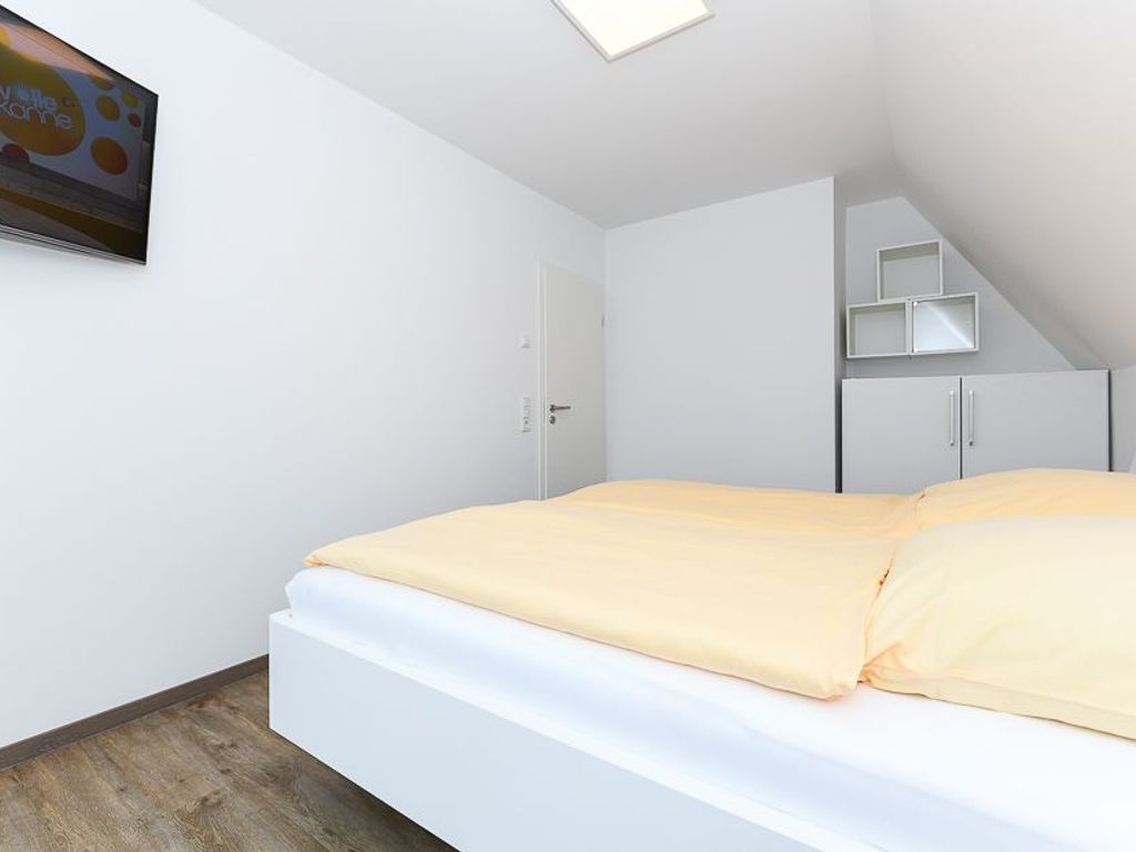 A bedroom with a bed, a door, a staircase, and a wall-mounted picture.