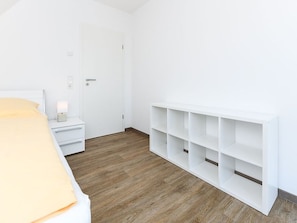 A bedroom with a bed, bedside table, nightstand, and a white shelving unit.