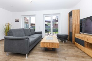 Un salon moderne avec un canapé gris, une table basse en bois et un meuble TV doté d’étagères en verre.