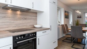 A modern kitchen with white cabinets, a wooden countertop, a built-in oven, and a dining area with a table and chairs.