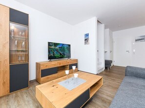 A modern living room with a wooden dining table, a flat-screen TV, and a grey sofa. - Vacation Home in Meer, Germany (Dornum)