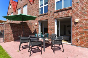 A brick building with a patio area featuring a table and chairs, a green umbrella, and a door leading to an interior space. - Vacation Home in Meer, Germany (Dornum)