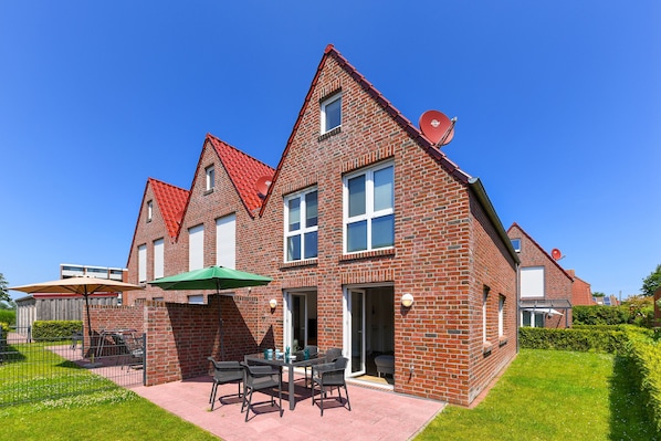 A two-story brick house with a red-tiled roof, a patio with outdoor furniture, and a satellite dish.