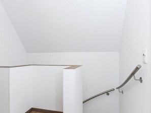A white interior space with a wooden floor and a metal handrail against the wall.