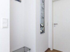 A hallway with a white door, a metal rack, and a vertical artwork on the wall. - Vacation Home in Meer, Germany (Dornum)