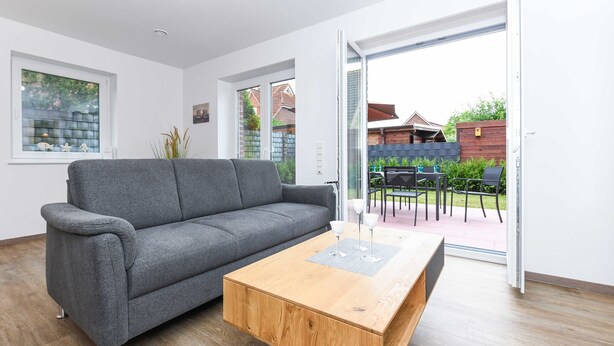 A modern living room with a grey sofa, a wooden coffee table, and a sliding glass door leading to an outdoor patio.