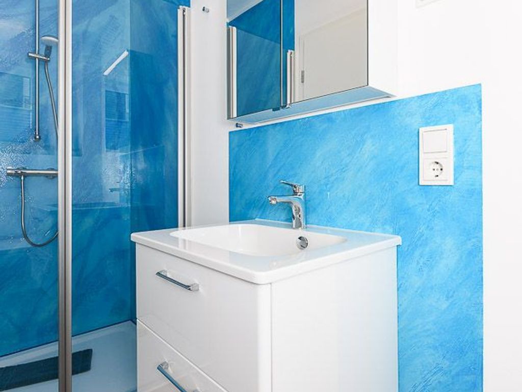 Un baño con lavamanos blanco, un espejo encima y zona de ducha con puertas de cristal.