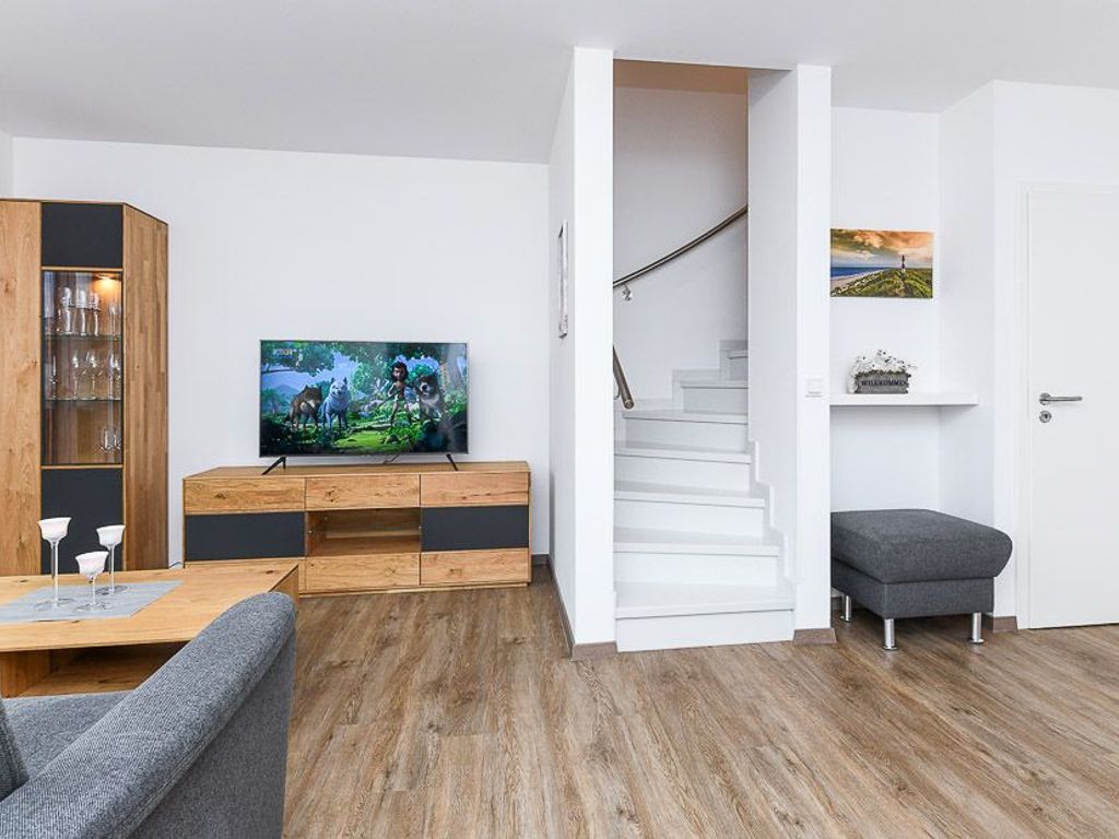 A modern living room with a flat-screen TV, wooden furniture, a staircase, and a door with a landscape painting.
