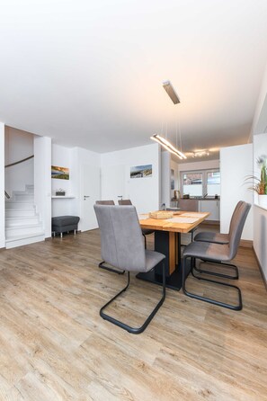 Une cuisine moderne avec une table et des chaises en bois, un escalier et une vue sur l’extérieur.