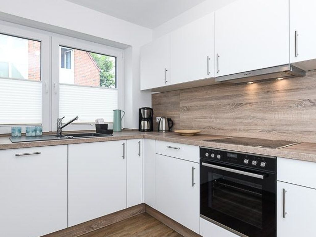 A modern kitchen with white cabinets, a wooden countertop, a built-in oven, and a window providing natural light.