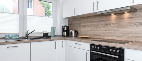 A modern kitchen with white cabinets, a wooden countertop, a built-in oven, and a window providing natural light.
