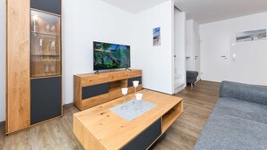 A modern living room with a wooden coffee table, a grey sofa, and a TV on a wooden cabinet.