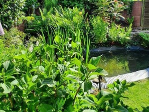 A lush garden with a pond, various plants, and a brick wall in the background. - Vacation Home in Korn am Bärensteig - FH for up to 6 people Patio + balcony, (Bruchweiler-Bärenbach)