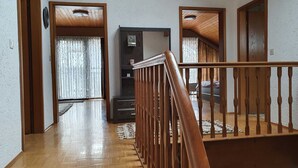 Una escalera de madera con barandilla que lleva a un rellano. Se ve una puerta de madera y una ventana con cortinas a la izquierda.