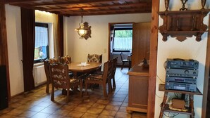 Un comedor con mesa y sillas de madera, una araña y una estantería con equipo de audio.