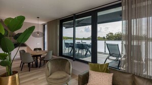 Una sala de estar moderna con un gran ventanal corredero que da a una terraza exterior con vista a un cuerpo de agua.
