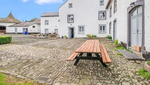 Ein Innenhof mit Kopfsteinpflaster, einem Holztisch und weißen Gebäuden mit grauen Fensterrahmen.