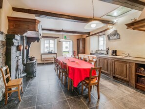 A dining area with a red tablecloth, wooden chairs, a bench, and a kitchen with a sink and cabinets. - Heritage Holiday Home in Gouvy with Fenced Garden (Gouvy)