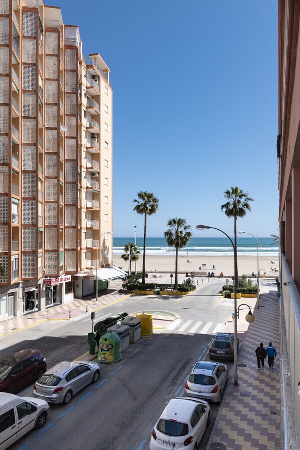 A coastal street with a beach view, parked cars, and a multi-story building with balconies. - ESTRELLA, 2º-10 (Cullera)